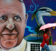 Una mujer pasa por una pintura del papa Francisco en Villavicencio, donde dará la misa durante su visita a Colombia. AFP