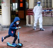 Un niño, que lleva un tapabicas, pasa frente a un oficial de policía que usa equipo de protección frente a la casa Hong Mei, en Hong Kong. AFP