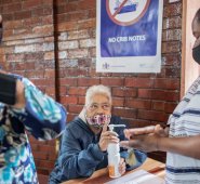 Un miembro del personal de la Escuela Secundaria Coronationville (centro), en Sudáfrica, desinfecta las manos de una mujer durante una distribución de alimentos y productos antes de Navidad. AFP