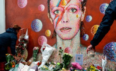 Personas ponen flores delante de un mural del cantante británico David Bowie, pintado por el artista callejero australiano James Cochran, tras el anuncio de la muerte de Bowie en Brixton, al sur de Londres. AFP