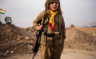En esta imagen aparece una niña kurda usando el rifle de asalto y el cinturón de municiones de un familiar, mientras espera en el puesto de control kurdo de la ciudad iraquí de Shaqouli, a unos 35 kilómetros al este de Mosul.  AFP