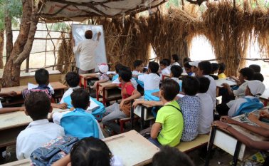 En una improvisada aula un grupo de estudiantes atienden las enseñanzas de un profesor protegidos por árboles y costales. AFP