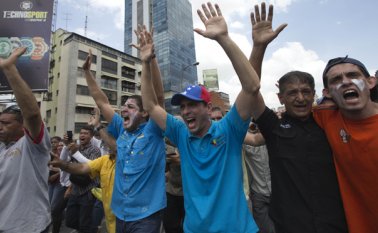 El gobernador del estado de Miranda y líder de la oposición Henrique Capriles levanta las manos junto con otros manifestantes pidiendo a la Guardia Nacional Bolivariana que deje de disparar gases lacrimógenos durante una protesta en Caracas. AP