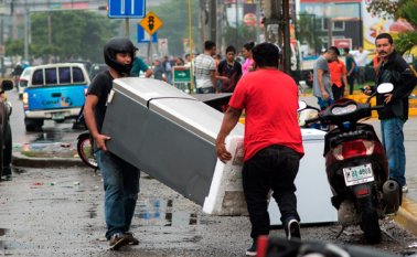 Hombres portan un refrigerador saqueado de una tienda, durante una jornada de caos en Honduras. AFP