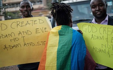 Una mujer que lleva una bandera del arco iris camina entre los miembros cristianos de una iglesia que sostienen letreros anti-LGBTQ y cantan contra la homosexualidad después del veredicto del Tribunal Supremo de Kenia AFP