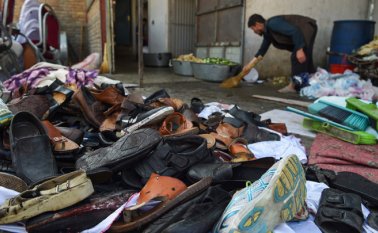 Un hombre limpia un área al lado de un montón de zapatos y sandalias de víctimas afuera del salón de bodas después de una explosión de bomba mortal en Kabul. AFP