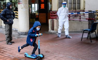 Un niño, que lleva un tapabicas, pasa frente a un oficial de policía que usa equipo de protección frente a la casa Hong Mei, en Hong Kong. AFP