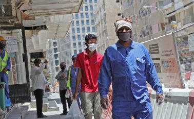 Trabajadores que usan máscaras protectoras caminan por una calle en la capital de Qatar, mientras el país comienza a aplicar las penas más duras del mundo por no usar máscaras en público. AFP