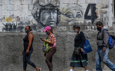 La gente usa máscaras faciales mientras camina junto a un mural que representa al difunto presidente Hugo Chávez, en el centro de Caracas. AFP