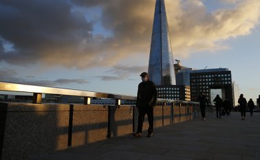 Un peatón con una máscara debido a la pandemia de coronavirus cruza el Puente de Londres con la torre Shard al fondo. AFP