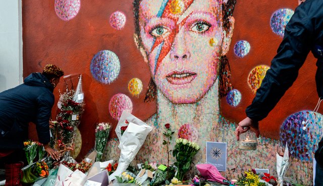 Personas ponen flores delante de un mural del cantante británico David Bowie, pintado por el artista callejero australiano James Cochran, tras el anuncio de la muerte de Bowie en Brixton, al sur de Londres. AFP