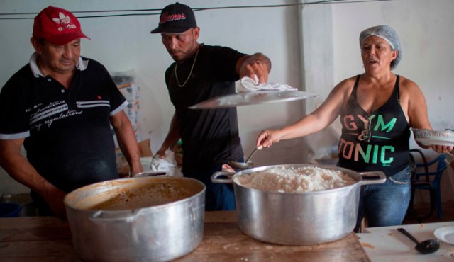 Un inmigrante venezolano (centro) ayuda a los barrios brasileños a preparar comidas para los refugiados venezolanos que viven en la Plaza Simón Bolívar, en Boa Vista, Roraima AFP