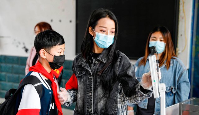 Un miembro del personal guía a un estudiante para verificar la temperatura corporal con un escáner térmico, antes de ingresar a una escuela primaria en Pingdingshan, en la provincia central china de Henan. China registró este domingo 13 nuevos casos de COVID-19. AFP
