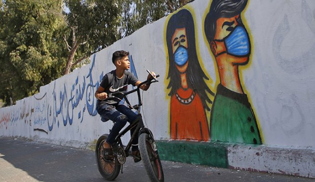 Un joven palestino pasa en bicicleta frente a un mural de concientización sobre el coronavirus en Deir Al-Balah en la Franja de Gaza AFP