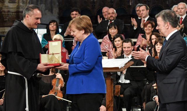 La canciller de Alemania Angela Merkel (centro) recibe el 'Nobel' católico por "su trabajo de conciliación para la convivencia pacífica de los pueblos", de Mauro Gambetti (izquierda), Guardián del Sacro Convento, y de Juan Manuel Santos, ganador del reconocimiento en 2016. AFP